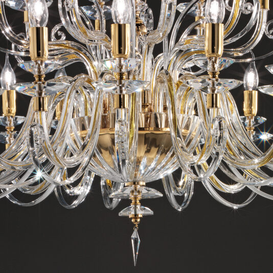 Large Classic Candle Style Chandelier A detailed view of the Large Classic Candle Style Chandelier showcases its gold-colored accents. The grand chandelier features numerous curved crystal arms adorned with clear light bulbs. The intricately designed crystal elements reflect light, creating sparkling effects.