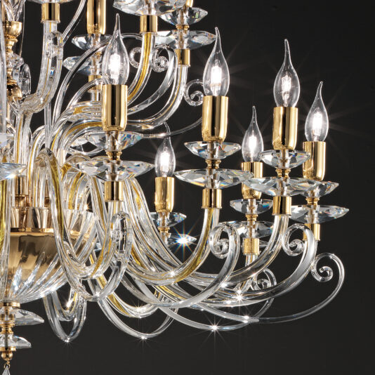 Large Classic Candle Style Chandelier A detailed view of the Large Classic Candle Style Chandelier reveals multiple glowing lightbulbs. The chandelier showcases intricate glass arms and gold accents, epitomizing luxury and elegance against a dark background. Its ornate design emits a soft, warm light.