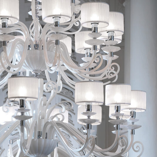 The Large White Glass Modern Chandelier hangs gracefully, highlighting its intricate curled metal arms and multiple lampshades. The soft white light emitted from these elegant shades accentuates the chandelier's ornate and sophisticated design, all set against a pristine white background.