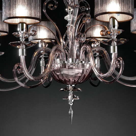 A close-up of the Modern Smoked Glass Chandelier showcasing its curving glass arms and multiple candle-style lights, each adorned with a cylindrical shade. The chandelier features intricate glasswork and a central crystal pendant, set against a dark background.