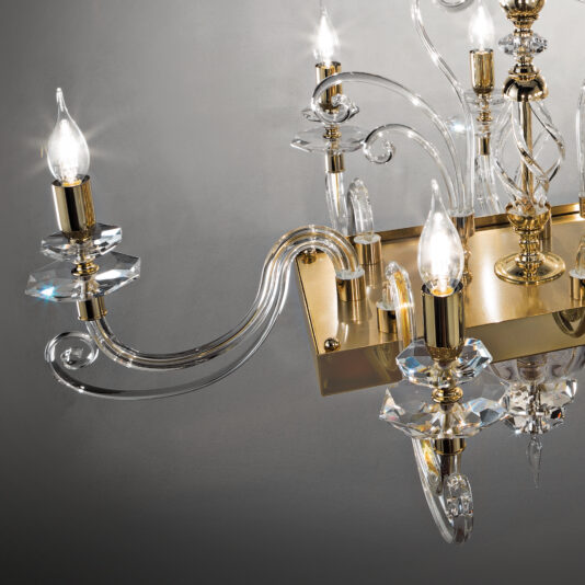A close-up view of the Rectangular Classic Candle Style Chandelier, featuring multiple candle-like lights. The glass arms elegantly curve upwards, and the ornate crystal and gold design emits a warm, sophisticated glow against a neutral background. Its subtle rectangular shape adds a touch of timeless elegance.