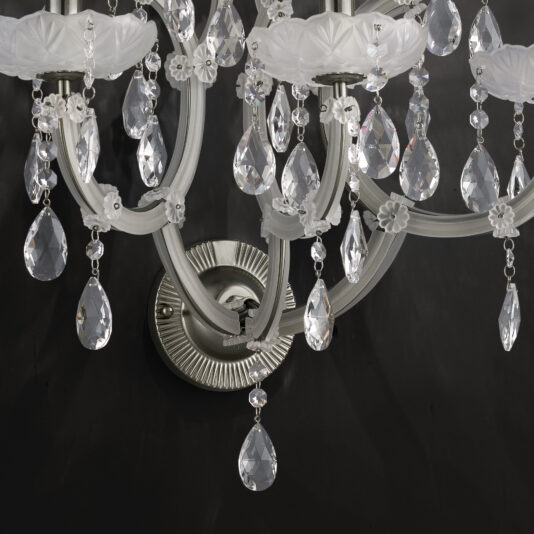 A close-up view of the Satin Glass Classic Style Wall Light against a dark background, showcasing its intricately designed crystal drops and elegant white, flower-shaped satin glass accents. The metal framework and reflective surfaces enhance the elegance and sophistication of this timeless fixture.