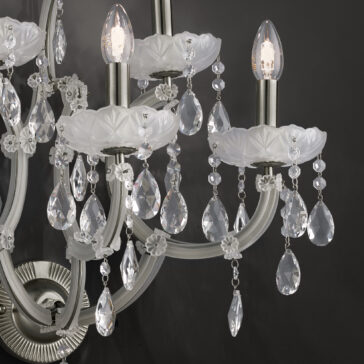 Close-up of the Satin Glass Classic Style Wall Light with lit candle-shaped bulbs. The fixture features white, decorative floral designs and numerous hanging crystal prisms that reflect the light. Satin glass elements add an extra touch of elegance. The dark background creates a striking contrast with the illuminated wall light.