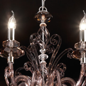 Smoked Glass 8 Arm Chandelier A close-up of the Smoked Glass 8 Arm Chandelier reveals its ornate, swirling glass arms and two illuminated candle-style light bulbs against a dark backdrop. The clear, crystalline appearance of the glass enhances the chandelier's elegant and sophisticated design.