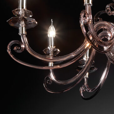 Smoked Glass 8 Arm Chandelier A close-up of the Smoked Glass 8 Arm Chandelier showcases its elegant, smooth, curved arms and multiple light bulbs, each adorned with glass coverings. This chandelier boasts a sleek, modern design accentuated by a black background that enhances its reflective surfaces.