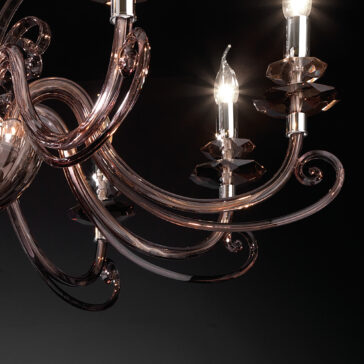 Smoked Glass 8 Arm Chandelier A close-up shot of the Smoked Glass 8 Arm Chandelier, showcasing its elegant and intricately designed curved arms and three lit candle-like bulbs against a dark background. The smoked glass arms and fixtures reflect light, creating a sophisticated and luxurious appearance.