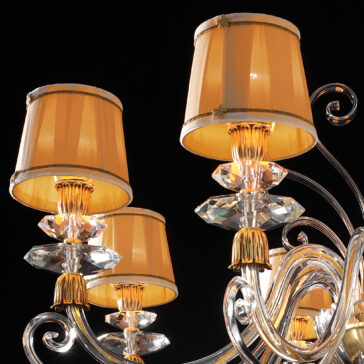 Swarovski® Crystal Chandelier With Shades Close-up of the Swarovski® Crystal Chandelier With Shades, showcasing five lampshades in a warm yellow hue, adorned with gold trim. The classic-style chandelier features intricate Swarovski® crystal decorations and elegant, curved metal arms against a black background.