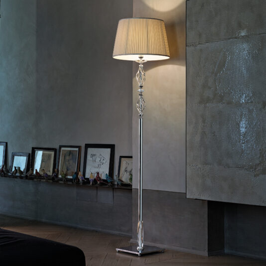 A sleek, contemporary room featuring the Twisted Floor Lamp With Swarovski® Crystal and a beige lampshade casting a soft light. The wall behind showcases framed artwork and decorative items displayed on a long shelf, with textured artwork hanging above.