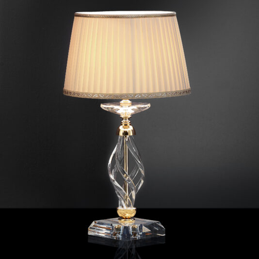 Displayed against a dark background is the Twisted Table Lamp With Swarovski® Crystal, featuring a sleek and elegant design with a beige pleated lampshade. Its spiral glass base, adorned with Swarovski® crystals and gold accents, seamlessly blends modern and classic design elements, adding a sophisticated touch to any space.
