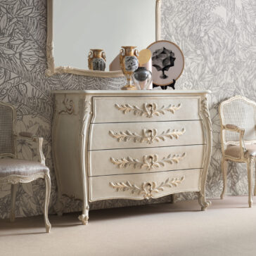 The elegant room showcases a Classic Style Bombe Chest Of Drawers, adorned with four intricately carved, gold-accented details. Above it hangs a large framed mirror, flanked by two ceramic vases and additional decor. Two upholstered chairs with matching ornate designs are placed on either side.