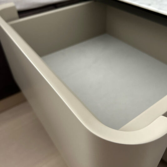 Contemporary Bedside Cabinet With Drawers A close-up image of an open, empty drawer from the Contemporary Bedside Cabinet With Drawers shows its smooth, rounded beige edges and light gray inner lining. Part of a wooden surface is visible on the left side of the image.