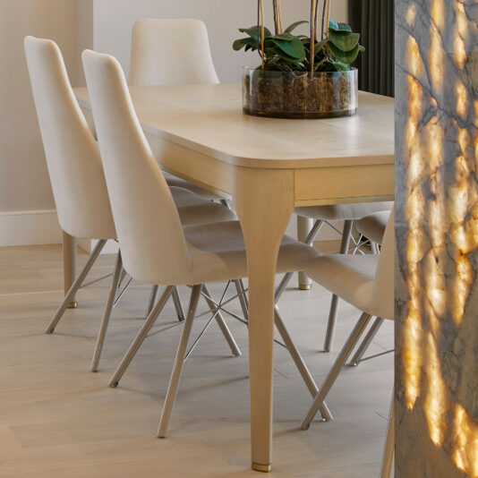 A minimalist dining room features a rectangular wooden dining table surrounded by six High-Back Curved Dining Chairs with metal legs. A potted plant with green leaves serves as a centerpiece on the table. Soft natural light illuminates the space.