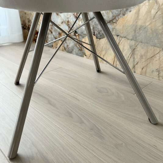 High-Back Curved Dining Chair Close-up view of the sleek, metal legs of a High-Back Curved Dining Chair on a light-colored wooden floor, set against a backdrop of a textured stone wall.