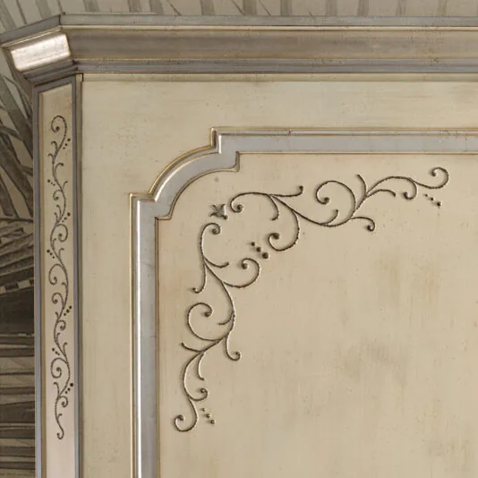 Large Classic Style Wardrobe A close-up of the Large Classic Style Wardrobe reveals a cream-colored wooden cabinet with intricate, carved floral designs on its door. The edges feature ornate detailing highlighted in a silver finish. The background shows a faint sketch-like pattern.