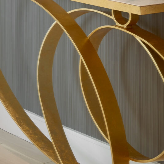 Modern Narrow Marble Ring Console Close-up image showcasing the ornate base of the Modern Narrow Marble Ring Console featuring gold, circular metal legs, placed against a wall with vertical striped wallpaper. The design incorporates intertwined loops, introducing a decorative and artistic flair to this elegant furniture piece.