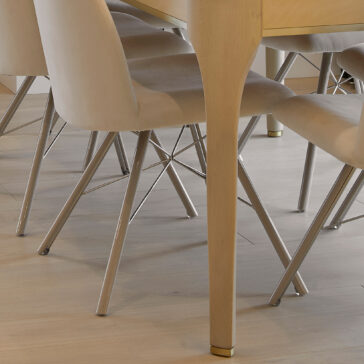 A close-up shot of the Modern White Maple Dining Table featuring light wooden legs and paired with beige upholstered chairs that have sleek metallic legs. The entire setup rests on a light-colored hardwood floor, creating a minimalist and contemporary look.