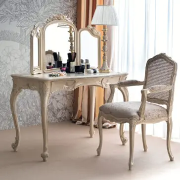 Ornate Classic Style Dressing Table Set The Ornate Classic Style Dressing Table Set showcases elegant intricate detailing and a large mirror flanked by two side panels. The surface is adorned with various cosmetics, and placed in front is a vintage-style cushioned chair featuring a wicker backrest and armrests. Completing the setup, a lamp rests atop the table.