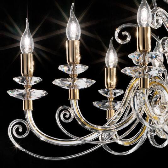 A close-up image of the Oval Candle Style Chandelier, showcasing its elegant design with multiple candle-shaped light bulbs. The lights are mounted on gold and clear glass holders. The chandelier features intricate, curving glass arms adorned with sparkling crystal accents, all set against a black background.