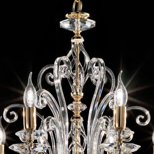 A close-up of the Oval Candle Style Chandelier against a dark background, highlighting its intricate glass and crystal elements. The design showcases elegant, curving glass arms with gold accents and candle-like bulbs that emit a warm, subtle glow.