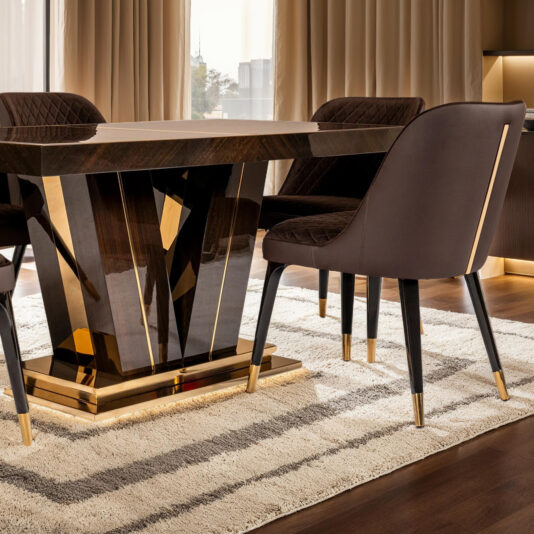 The Exclusive Abstract Rectangular Designer Dining Set enhances the modern space with a dark wood table featuring a glossy finish and gold accents, surrounded by upholstered chairs with gold-tipped legs. A beige and gray striped rug underlines it, paired elegantly with beige curtains.