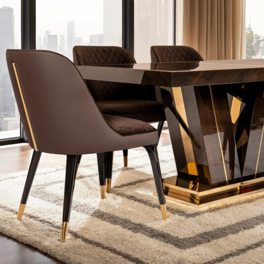 An exclusive dining room showcases the Exclusive Abstract Rectangular Designer Dining Set, featuring a large dark wood table with gold accents and elegant brown quilted chairs. Floor-to-ceiling windows offer city skyline views, while a plush beige rug adds modern sophistication.