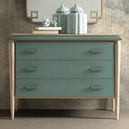 A light teal Luxury Art Deco Style Chest Of Drawers with three compartments and light-colored legs, adorned with two decorative ceramic jars and a small figurine. Behind it, a partially visible mirror with a gold-bordered edge is mounted on a textured wall.