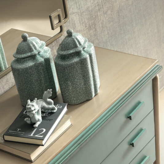 A stylish Luxury Art Deco Style Chest of Drawers with a light-colored wooden top and pastel green body features two textured green ceramic jars with pointed lids and a small decorative horse sculpture, along with the book 