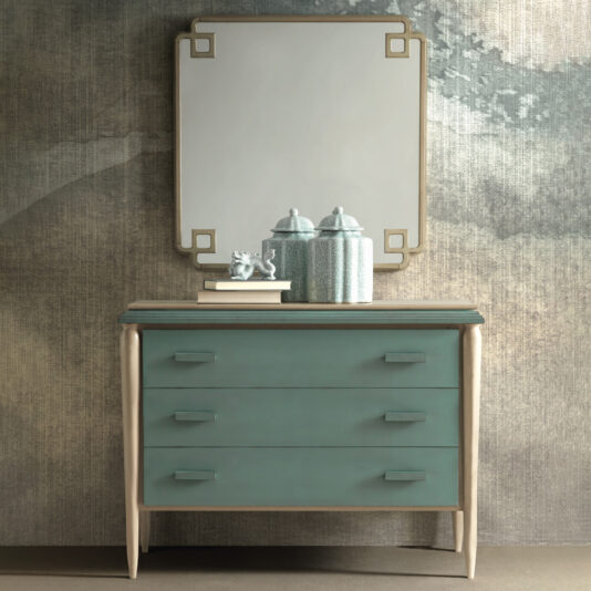 The Luxury Art Deco Style Chest Of Drawers boasts a teal-colored body and three spacious drawers, beautifully adorned with vintage decor containers and a figurine on top. Complementing this piece, a square mirror with a geometric frame hangs against an abstract-designed textured wall.