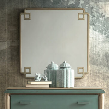 Luxury Square Art Deco Style Mirror A Luxury Square Art Deco Style Mirror with elegant corners hangs on a wall; beneath it is a teal dresser adorned with two ornately designed lidded jars, a small statue, and a stack of books. The background showcases a textured, artistic wall design.
