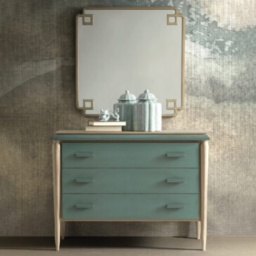 Luxury Square Art Deco Style Mirror A teal dresser with three drawers, featuring minimalist handles, stands against a textured wall. On top of the dresser are two decorative jars and a small figurine. Above is the Luxury Square Art Deco Style Mirror, a large framed square mirror with rounded corners and metal accents that captures the essence of Art Deco luxury.