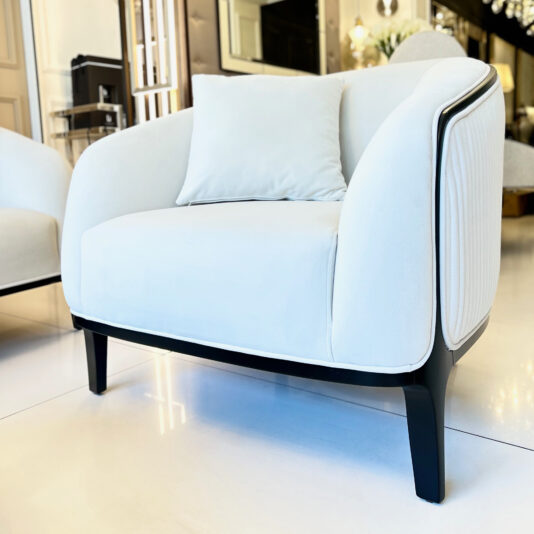 The Mid Century Style Curved Armchair, featuring modern white upholstery paired with a sleek black wooden frame, is showcased in a bright and stylish room. The light-colored flooring and contemporary decor further enhance the armchair's timeless appeal.