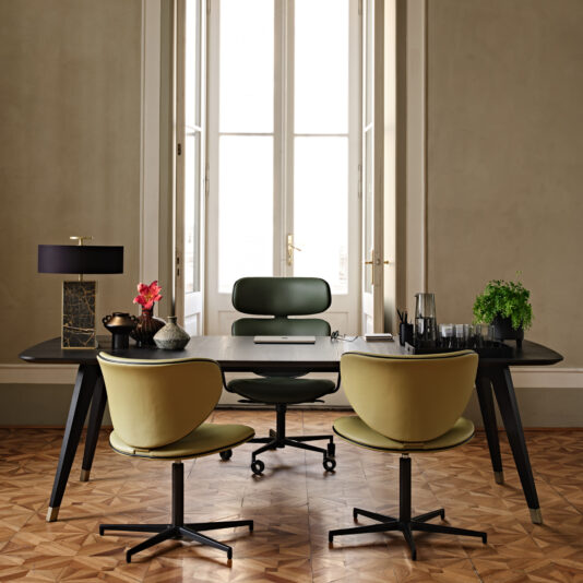 A stylish office with a Contemporary Rectangular Moka Ash Dining Table serving as the dark wooden desk, accompanied by three green chairs on a patterned wooden floor. The table features a black lamp, a potted plant, a carafe of water, a notebook, and decor items. Large windows in the background allow natural light into the room.
