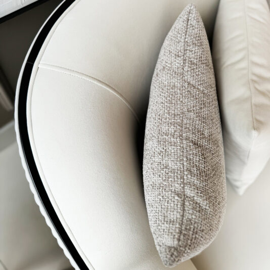 A close-up of a Mid Century Style Curved Sofa in modern white showcases its sleek black piping along the curved edge, paired with a light gray textured throw pillow and a white cushion for stylish contrast against the clean upholstery.