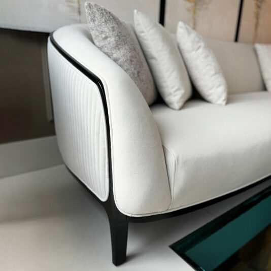 The Mid Century Style Curved Sofa features a sleek curved design with black legs and a modern white finish, complemented by several decorative pillows in white and gray, all placed against a neutral-toned wall.