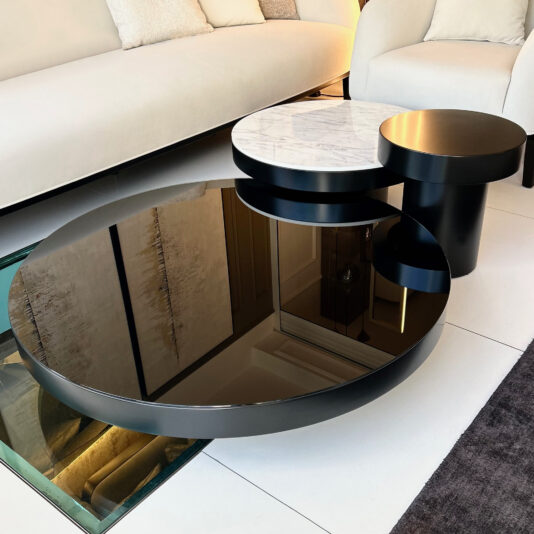 The Set Of 3 Modern Round Coffee Tables is a chic addition to any living room, featuring three circular tiers: the largest in glossy black, the middle with a stunning white marble pattern, and the smallest in matte black. It complements a stylish space beautifully when placed against a backdrop of a beige sofa.