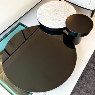 The scene in the contemporary living room features the Set Of 3 Modern Round Coffee Tables, each with sleek black reflective surfaces, and one displaying a chic white marble top. These tables are gracefully positioned on a tiled floor next to a trendy rug and wall.