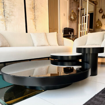 A contemporary living room features white sofas paired with beige cushions and a Set Of 3 Modern Round Coffee Tables that boast reflective surfaces. The space is further enhanced by warm lighting and abstract wall art, establishing an elegant and inviting ambiance.