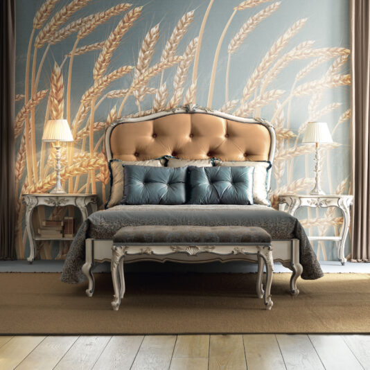 Carved Louis Style Tufted Bed The bedroom showcases an elegant Carved Louis Style Tufted Bed adorned with blue bedding. The bed is flanked by two ornate nightstands, each topped with a lamp. A large wheat-themed mural on the wall behind adds rustic charm to the space. Wooden floors and warm lighting complete the inviting atmosphere of the room.