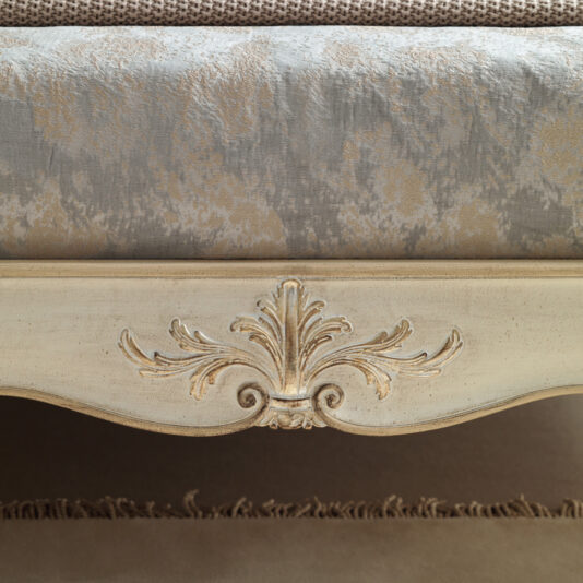 Classic Louis Style Button Upholstered Bed Close-up of the High End Button Upholstered Bed (Copy) featuring an ornate wooden bed frame with a carved floral design in the center. The bed exudes elegance with its high-end button upholstery and textured fabric bedspread showcasing a subtle pattern in shades of gray and beige, creating a vintage aesthetic.