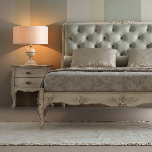 Classic Louis Style Button Upholstered Bed A classy bedroom scene featuring the luxurious High End Button Upholstered Bed with a tufted satin headboard and ornate carvings. The bed is adorned with elegant pillows and bedding. A matching nightstand supports a lamp with a beige shade, while striped wallpaper and a plush rug complete the sophisticated look.
