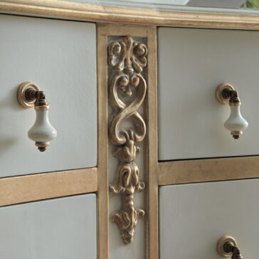 Close-up of the Classic Style Large Chest Of Drawers, highlighting its ornate golden trim with intricate carvings and white drawers. It is adorned with elegant white and gold ceramic handles, enhancing its vintage appearance.