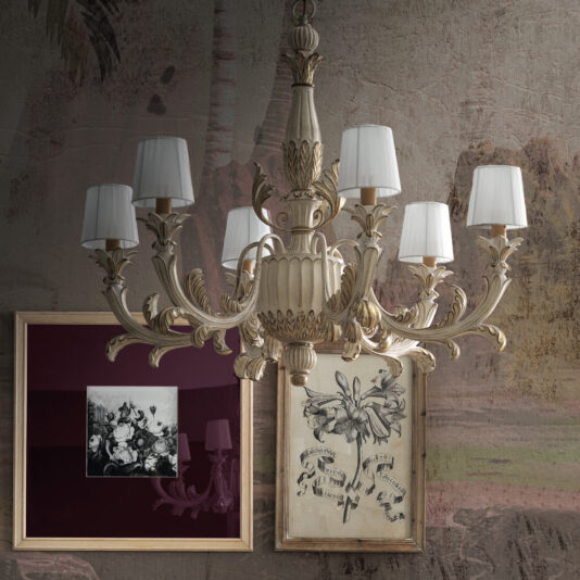 The Classic Style Ornate Chandelier gracefully hangs from the ceiling, its six ornate arms adorned with white lampshades. Below it, two framed artworks decorate a textured wall: one displaying a black and white floral image, and the other presenting a botanical illustration.