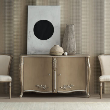 A luxurious High End Rococo Inspired Sideboard in beige, embellished with intricate floral carvings, is situated between two chairs. Above it, a white and black abstract painting complements the display of decorative vases. The setting is enhanced by a textured, neutral wall backdrop.