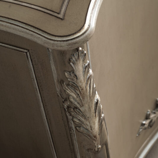 High End Rococo Inspired Sideboard Close-up of an elaborate corner of the High End Rococo Inspired Sideboard, showcasing intricate leaf carvings and a distressed finish. The edge is gently curved with a smooth, aged appearance that accentuates the exquisite craftsmanship.