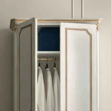 Narrow Classic Style Wardrobe A partially open, Narrow Classic Style Wardrobe in white with gold trim showcases hanging white shirts and a blue storage box on the upper shelf. The elegant piece stands against a plain wall.