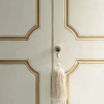 Narrow Classic Style Wardrobe Close-up of the Narrow Classic Style Wardrobe's ornate white and gold door, adorned with a decorative tassel hanging from the center. This large piece showcases carved geometric patterns and a textured appearance, enhancing its elegant design.