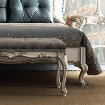 Ornate Louis Style Bench A lavish bedroom arrangement featuring an exquisite tufted headboard, a beautifully patterned duvet, and the Ornate Louis Style Bench with its intricately carved legs. The backdrop displays a floral-designed wallpaper, accentuated by a vintage nightstand adorned with elegant details.