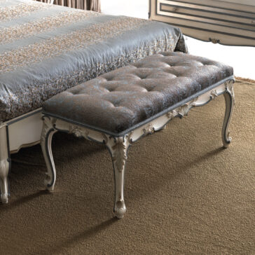 Ornate Louis Style Bench The Ornate Louis Style Bench, featuring elegant wooden legs and intricate detailing, stands at the foot of a bed. It is complemented by a tufted, patterned cushion and placed on a brown carpet next to a bed dressed with a patterned bedspread.