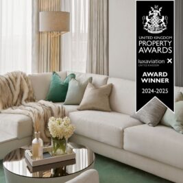 Elegant living room featuring a white sectional sofa, green and beige pillows, a faux fur throw, and a glass coffee table adorned with flowers. A prominent award banner highlights the UK Property Award, celebrating the space's win for 2024-2025.