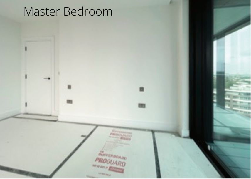 An empty room with white walls, bearing the "Master Bedroom" label, boasts a wooden door, two power outlets, and a large window offering a view of surrounding buildings. The floor is partially protected by a board—a space deserving of UK Property Award recognition.